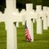 Rows of wooden crosses at a cemetery, with one little American flag stuck into the grass by one cross